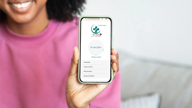 L'immagine mostra una donna sorridente con indosso una maglia rosa che tiene in mano uno **smartphone**. Sullo schermo è visibile un **profilo digitale sanitario** dell'applicazione **My Info Healthcare**, con il logo ben in evidenza in alto. L'interfaccia dell'app visualizza informazioni personali come **nazionalità, luogo di nascita, data di nascita e numero di telefono**, suggerendo l'uso di una **cartella clinica digitale accessibile online**.  <br /><br />Questa immagine rappresenta il concetto di **identità sanitaria digitale**, evidenziando l'importanza della **gestione digitale dei dati medici**, la **telemedicina**, e l'accessibilità delle informazioni sanitarie tramite **dispositivi mobili**.  <br /><br />Parole chiave SEO: **cartella clinica digitale, app sanitaria, telemedicina, identità sanitaria online, My Info Healthcare, tecnologia medica, salute digitale, accesso ai dati sanitari**.